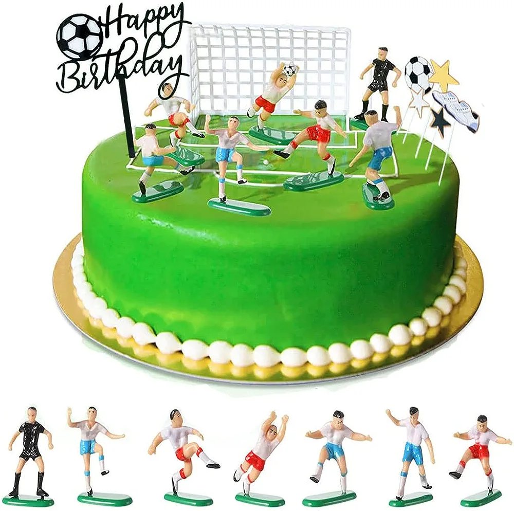 A round green birthday cake is decorated with a white icing border at the bottom. On top, there are several miniature soccer player figurines engaged in a game, with a small soccer goal set in the background. A black sign with the words "Happy Birthday" in cursive is also placed on the cake. In front of the cake, there are additional miniature soccer players posed in various actions. The scene is festive and themed around soccer, making it suitable for a birthday celebration.