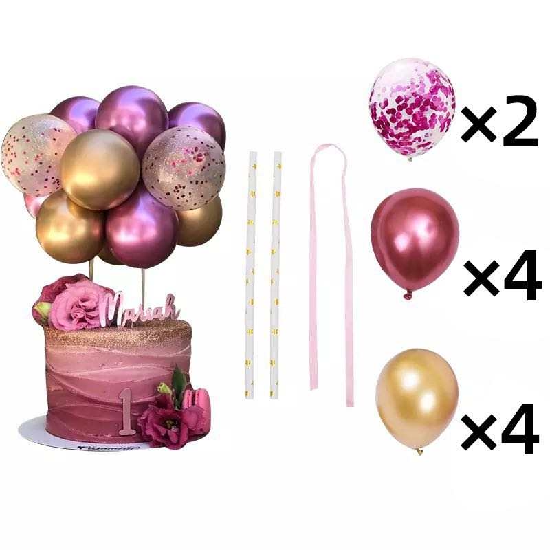 A cake decorated with pink ombre frosting and flowers, topped with a cluster of balloons in shades of pink, gold, and confetti. The set includes 10 pieces: two confetti balloons, four pink balloons, and four gold balloons, along with three balloon supports and a pink ribbon. The cake has a small sign reading "Mavah" and the number "1" on the side.