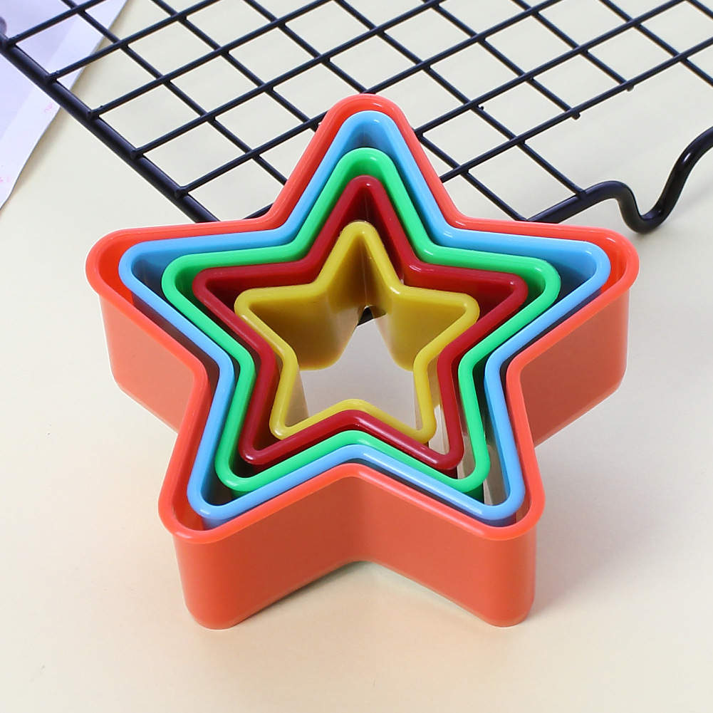 A set of five star-shaped cookie cutters stacked together. The cutters are made of flexible plastic and come in a variety of colors: red, green, blue, yellow, and orange. They are placed on a light-colored surface next to a black wire cooling rack.