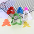 A set of five gingerbread man cookie cutters in various colors is displayed on a cooling rack. The cutters include red, blue, pink, green, and white. There are also two shaped cutouts in orange and yellow on a pale yellow surface next to the cutters. The arrangement showcases the playful design of the cookie cutters, ideal for making gingerbread man cookies.