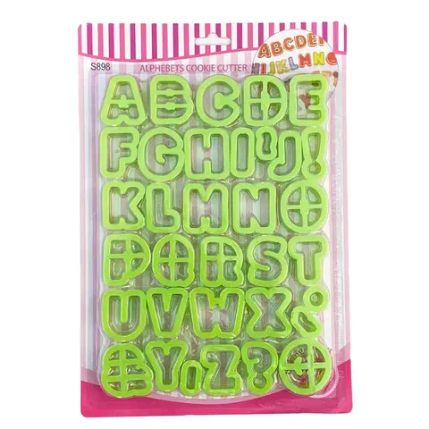 The image shows a packaging of plastic alphabet cookie cutters. The cookie cutters are shaped like letters and symbols from A to Z, including an exclamation mark and a question mark. They are bright green in color and are arranged neatly in the package. The packaging features a pink striped border at the top, with the words "Alphabets Cookie Cutter" displayed prominently. The overall design is colorful and playful, suitable for baking and decorating cookies.