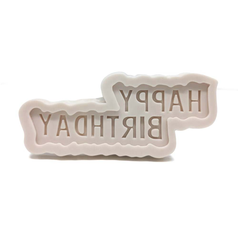 The image shows a silicone mold designed to create cake decorations. The mold features the phrase "HAPPY BIRTHDAY" in a bold, stylized typeface. The letters are indented and have a scalloped edge, giving them a decorative appearance. The mold is pale in color, likely light beige or white, and has a flexible, soft texture typical of silicone materials. The background is plain and white, emphasizing the mold&