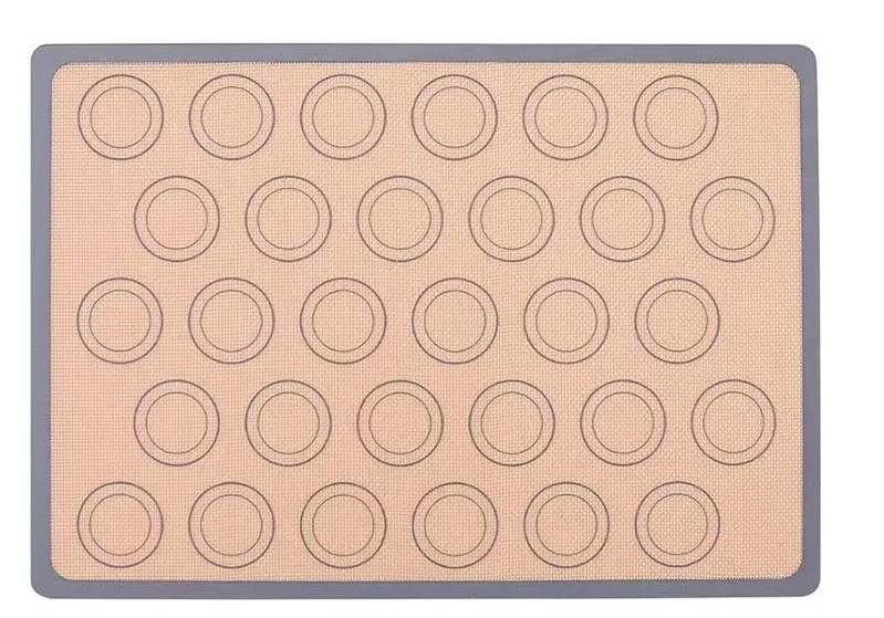 A silicone baking mat with multiple circular impressions for evenly spacing baked goods. The mat has a non-stick surface and is bordered by a gray edge. The background is a light tan color with a textured design.