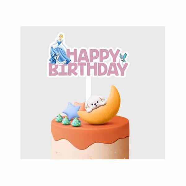 A colorful birthday cake adorned with a decorative topper. The topper features the phrase "HAPPY BIRTHDAY" in pink letters, along with a depiction of a character wearing a blue dress, a small seal, and a light orange crescent. The cake has a light beige base and is topped with orange frosting along with blue and green decorative elements.
