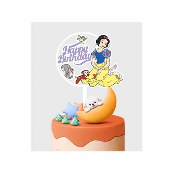 A colorful birthday cake topper featuring a character that resembles Snow White, surrounded by small animal figures, including a bird, a squirrel, and a rabbit. The topper includes the text "Happy Birthday" in playful lettering. The cake has an orange frosting layer with decorative elements like a blue star and small green icing decorations on top. There&