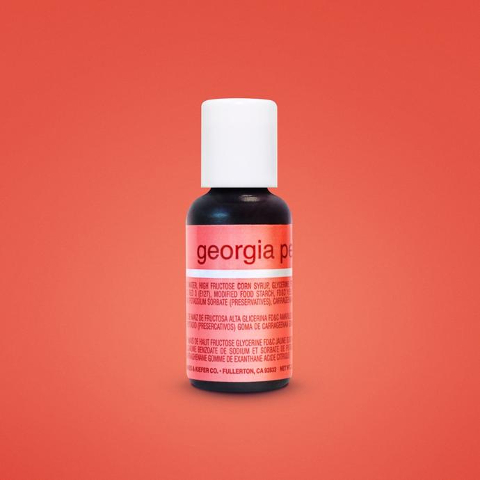 A small bottle of liquid food coloring is centered in the image against a solid orange background. The bottle, labeled "georgia peach," has a black body and a white cap. The label contains ingredient information and is predominantly pink with white text. The bottle is 0.7 ounces (20 ml) in size.