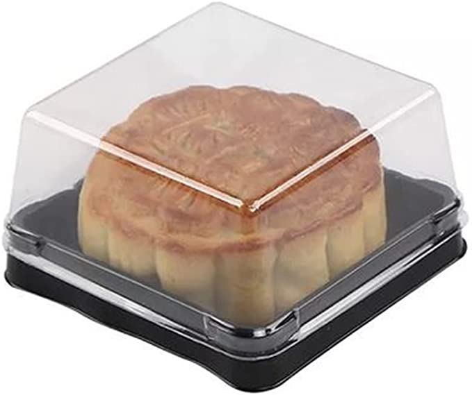 A clear plastic container with a black base, holding a single mini mooncake. The mooncake has a golden-brown crust with a decorative pattern on top. The container is slightly domed, allowing a view of the mooncake inside.