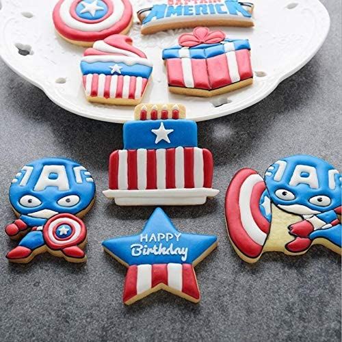 A collection of decorated cookies themed around Captain America, displayed on a white plate. The set includes a cookie shaped like Captain America in his costume, a birthday cake with red and white stripes and a blue star, a blue star with the text "HAPPY Birthday" in white, a red and white present, a cupcake with a red and white swirl, and a round cookie featuring Captain America&