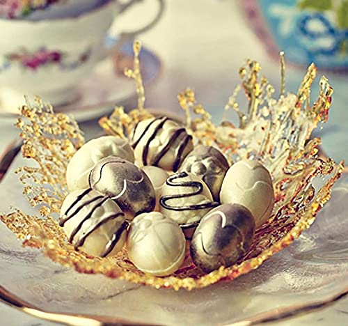 A decorative plate features an artistic arrangement of chocolate or candy eggs. The eggs are variously colored in light and dark shades, with some adorned with a glossy finish and intricate designs, including stripes and patterns. They are nestled in a delicate, golden, lace-like bowl or dish, enhancing the overall presentation. The background includes soft, blurred floral patterns and a hint of a teacup, suggesting a refined setting.