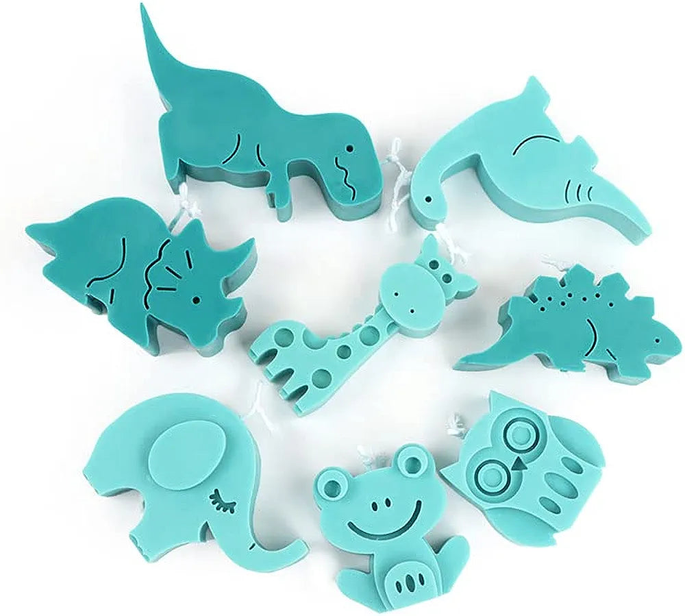 The image shows a collection of teal silicone molds shaped like various animals and dinosaurs. The molds include the following designs: a dinosaur (T-Rex), a triceratops, a giraffe, an elephant, a frog, an owl, a stegosaurus, and several other animal shapes. Each mold features simple, cartoonish details, with some showing facial features like eyes and mouths. The molds are arranged in a scattered pattern on a light background.