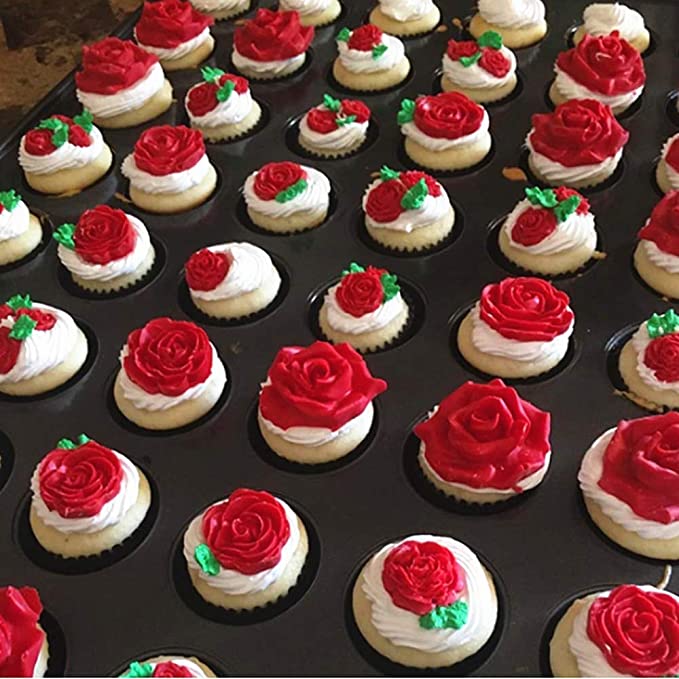 A tray filled with decorative cupcakes, each topped with frosting and detailed floral designs. The cupcakes feature vibrant red roses made from icing, some accompanied by green leaves and additional small red accents. The arrangement showcases a variety of decorated cupcakes, combining smooth white frosting with the bright red rose designs.