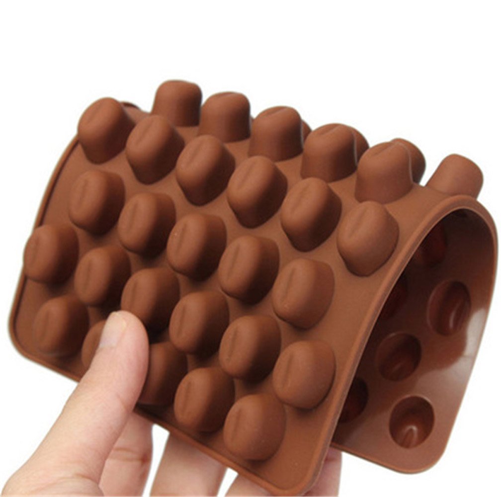 A hand holds a brown silicone mold shaped like coffee beans, featuring multiple rounded cavities resembling the form of coffee beans. The mold is slightly curved, showcasing rows of bean-shaped impressions on its surface.