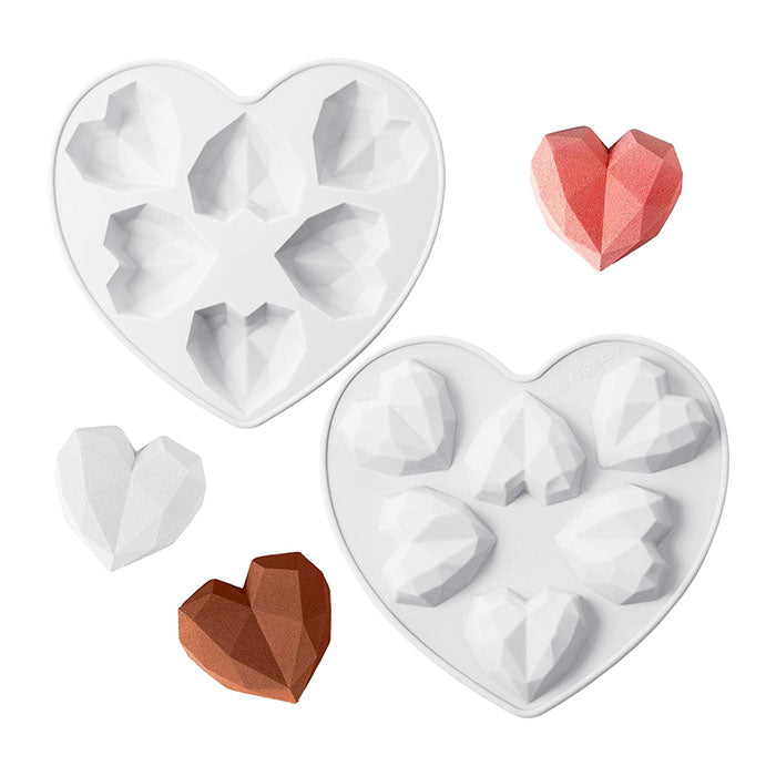A heart-shaped silicone mold with several diamond-shaped cavities, designed to create heart-shaped items. The mold is white and features multiple small heart shapes. Surrounding the mold are three finished heart-shaped items in different colors: a white heart, a brown heart, and a pink heart, all resembling diamond shapes.