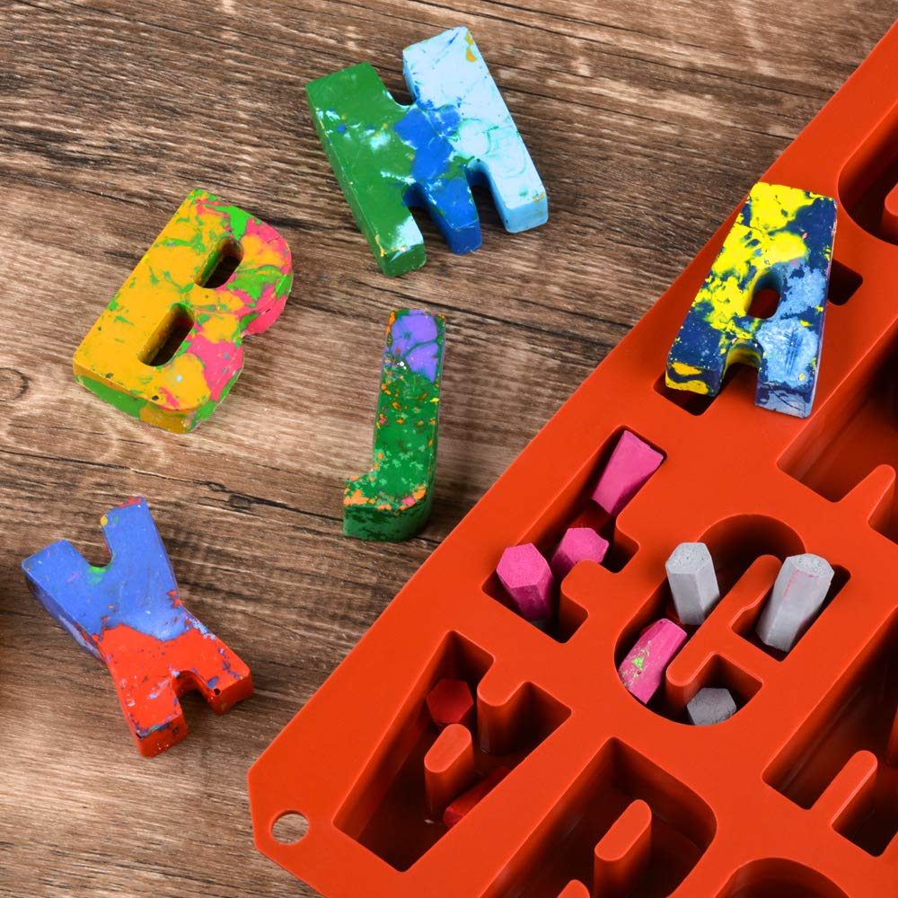 An orange silicone mold in the shape of uppercase letters is displayed on a wooden surface. Some colorful letters made from crayon-like materials are scattered around the mold. The visible letters include a yellow "B," a green "J," a blue "H," and a purple "K." The letters feature vibrant colors with speckles and patterns. Inside the mold, various colored shapes are seen, including pink and gray pieces forming letters. The overall scene conveys a playful and creative atmosphere.