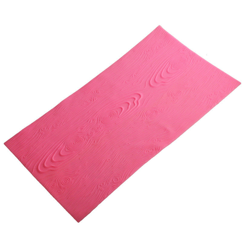 A pink silicone mat with an impression design resembling wood grain. The mat is rectangular, showcasing detailed patterns that mimic the texture and lines of wood, suitable for use in cake decorating and fondant applications.
