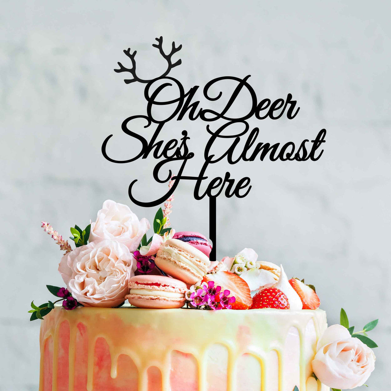 A colorful cake topped with an acrylic cake topper that reads "Oh Deer She&