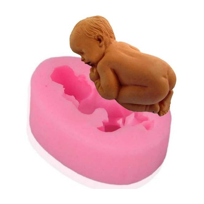 A pink silicone mold shaped like a heart is displayed, with an intricately detailed miniature figure of a naked baby positioned on top. The baby appears to be in a curled-up pose, highlighting its features against the mold. The pink mold has a cavity that resembles the baby, ready for casting or crafting purposes.
