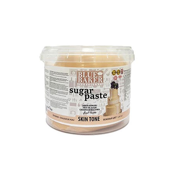 An image of a plastic container labeled "Blue Baker Sugar Paste" in a skin tone shade. The container has a transparent lid and features an image of a decorated cake on the front. The text prominently displays "sugar paste" and "skin tone." Additional product information is located on the side of the container. The container holds 1 kg of fondant.