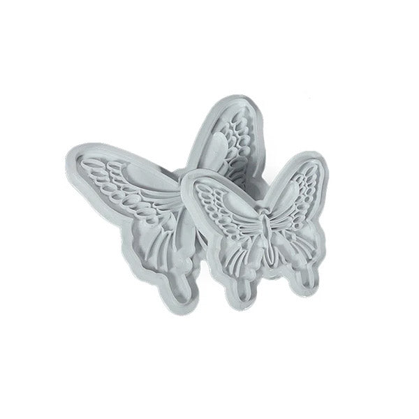 A set of two butterfly-shaped cutters made of white material. The cutters are intricately designed, showcasing detailed wing patterns and shapes. One cutter is slightly larger than the other, both positioned close together.