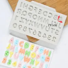 A silicone mold for mini domed alphabet and numbers, featuring an array of letters and numbers on a white background. The mold includes uppercase letters A-Z and numbers 0-9. The letters and numbers have a rounded, three-dimensional appearance, and are shown alongside colorful, completed letter and number shapes in various pastel colors. A wooden surface is partially visible behind the mold.
