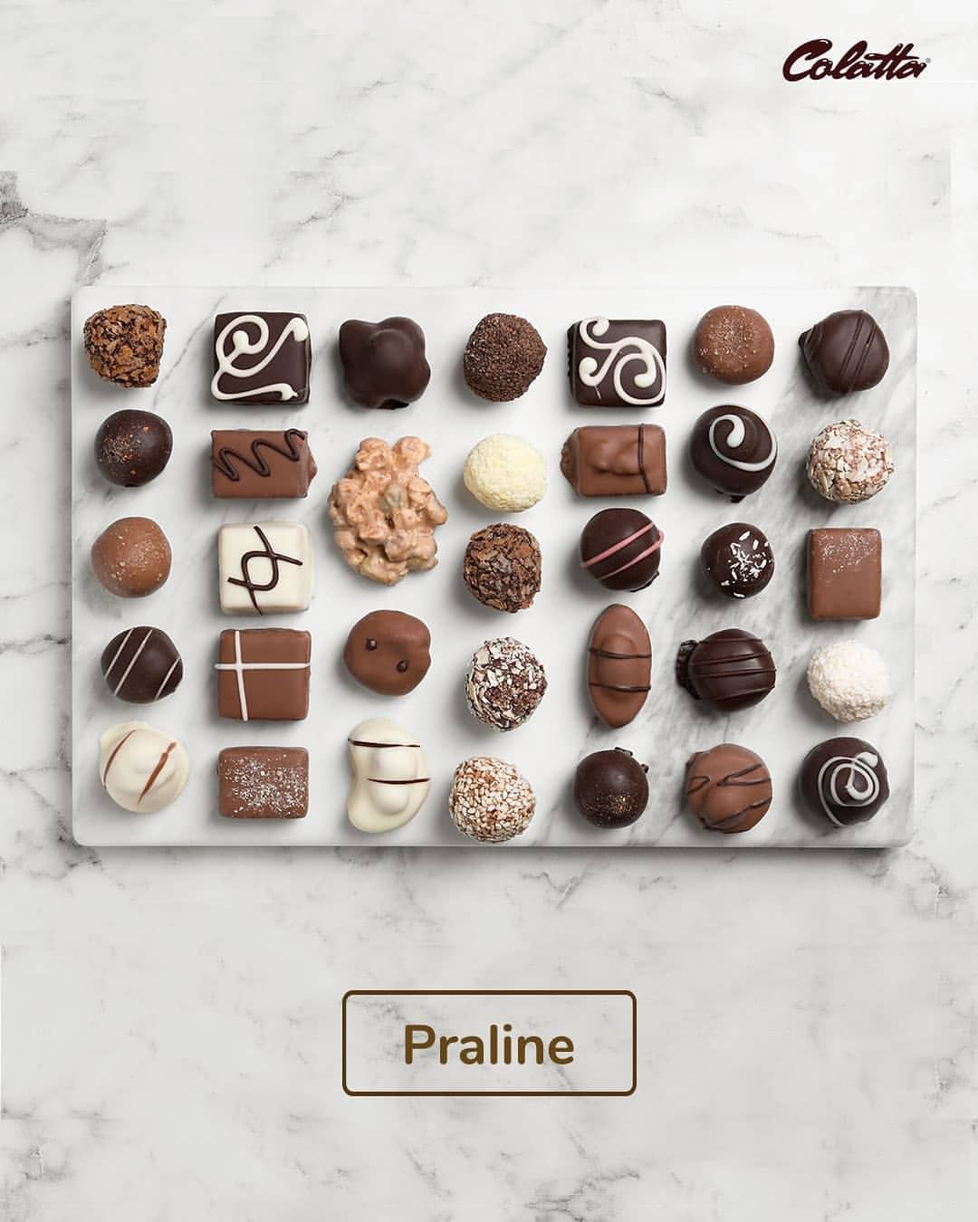 A flat lay of assorted chocolates on a white marble surface. The chocolates vary in shape and design, including pralines, truffles, and coated bites, featuring different types of chocolate, drizzles, and toppings. The word "Praline" is displayed in a gold box at the bottom of the image. The Colatta logo is visible in the top right corner.