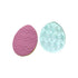 Two egg-shaped cookie stamps are displayed side by side. The left stamp is pink with a zigzag pattern and small raised dots. The right stamp is translucent blue with a similar zigzag design and raised lines. Both stamps are designed for embossing fondant, particularly for Easter-themed baking.