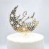 An elegant acrylic cake topper featuring a crescent moon design adorned with geometric star patterns, with the words "Eid Mubarak" artistically displayed. The topper is gold in color and is placed atop a white, round cake. The background is plain, enhancing the focus on the decorative piece.