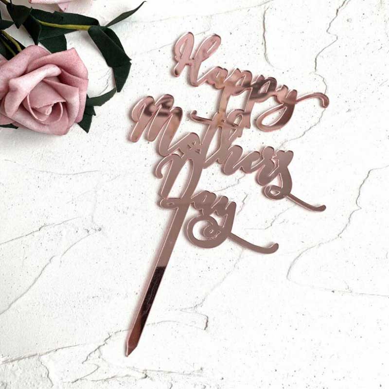 A rose gold acrylic cake topper that reads "Happy Mother&