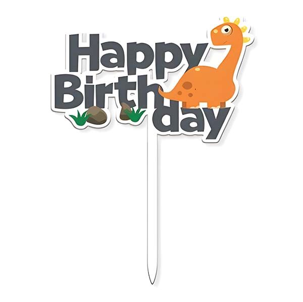 A colorful birthday cake topper featuring the text "Happy Birthday" in bold letters. The word "Happy" is in black, while "Birthday" is in gray. An orange dinosaur character is positioned to the right, with small rocks and green grass illustrations below the text. The topper has a white stick for placement in a cake.