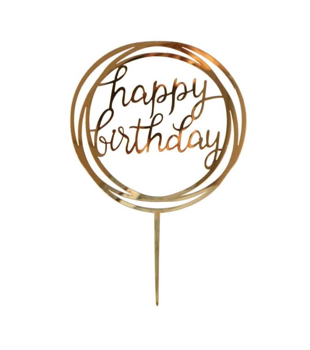 A gold-colored cake topper featuring the words "happy birthday" in a decorative script. The text is enclosed within a circular design, giving it an elegant appearance. The topper has a pointed base for inserting into a cake.