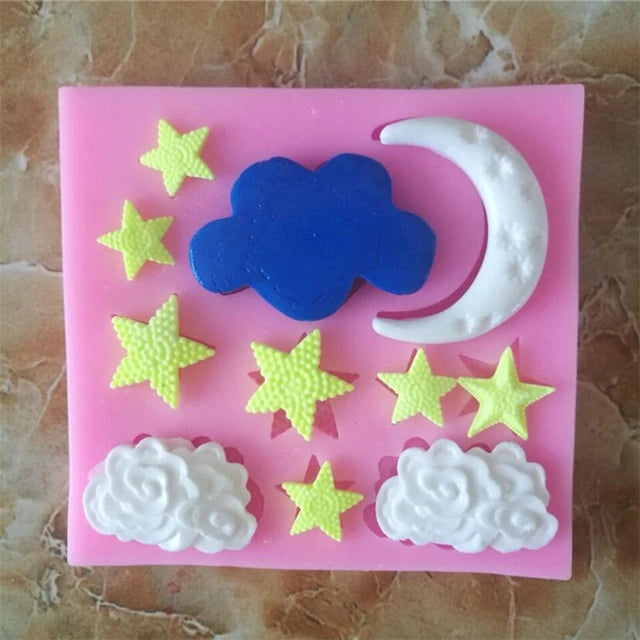 The image depicts a pink silicone mold featuring various designs. There are three white clouds at the bottom, a blue cloud in the center, a crescent moon in the upper right, and multiple stars in shades of yellow and green scattered throughout the mold. The designs are raised and textured, ideal for creating decorative items.