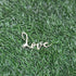A customized cake topper featuring the word "love" in an elegant, cursive font. The topper is displayed on a background of green artificial grass. The design is simple and decorative, suitable for cake decoration.