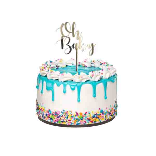 A round cake with a white base features blue frosting drizzled down the sides. The top is adorned with a ring of white whipped cream and colorful sprinkles. At the center of the cake, a gold acrylic topper reads "Oh Baby," standing upright on a stick. The cake is displayed on a round cake board, and the overall appearance is festive and celebratory.