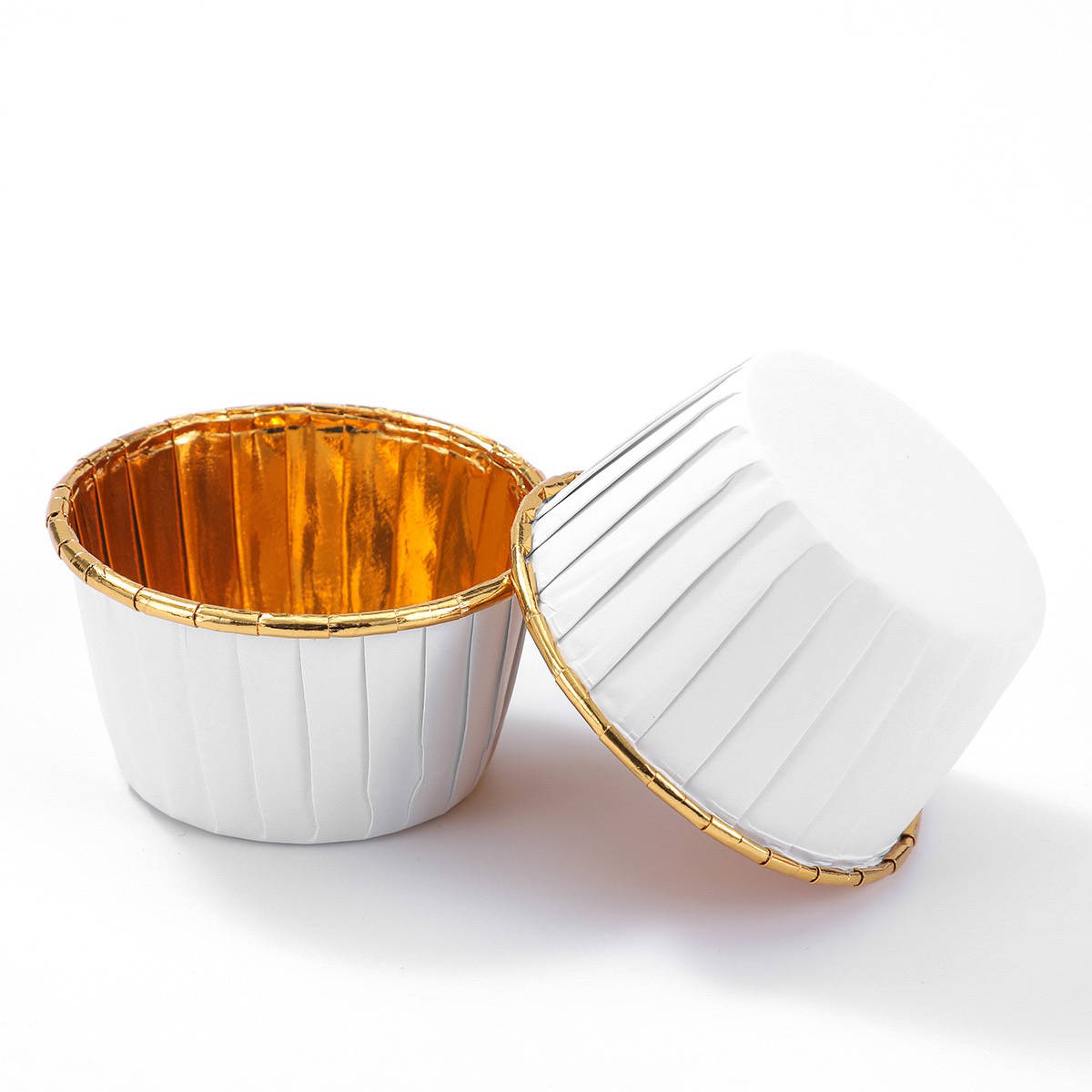 Two aluminium foil ramekins are displayed, one upright and one tilted. The ramekins have a shiny gold interior and a white exterior with pleated sides. They appear lightweight and are designed for baking purposes. The background is plain and white, highlighting the ramekins.