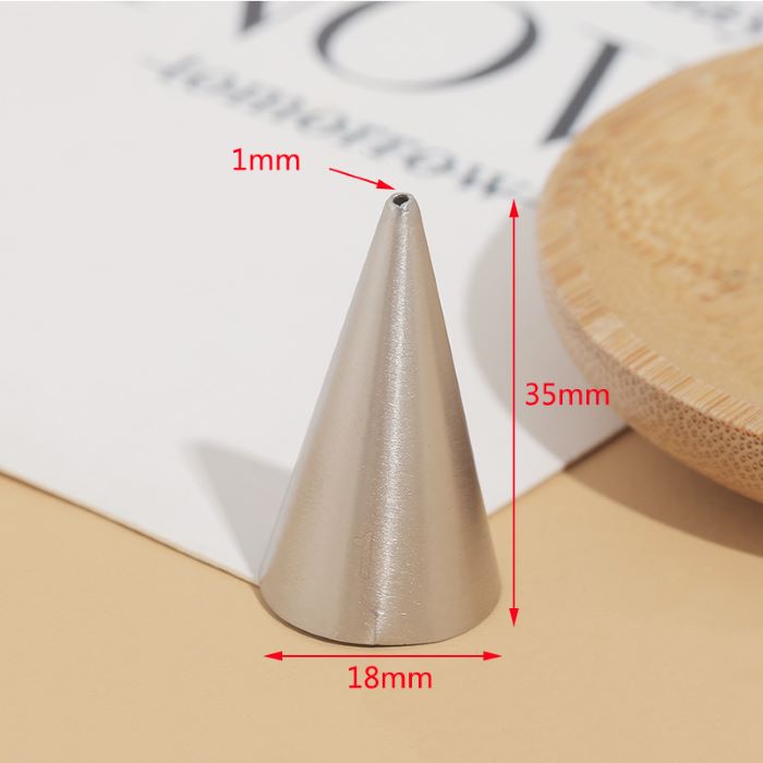 "A metallic piping nozzle with a pointed tip, measuring 1mm at the opening, 35mm in height, and 18mm in diameter at the base. The nozzle is placed on a flat surface with a light background, alongside a wooden plate and partially visible text on paper."