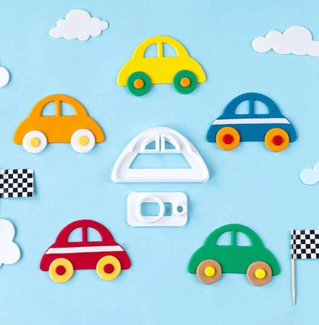 The image features several car-shaped cookie cutouts made from colorful materials, arranged on a light blue background. There are five car shapes in red, yellow, green, blue, and orange, each with distinctive details, such as windows and wheels. In the center, there?s a white cookie cutter in the shape of a car, along with a few decorative elements, including two white clouds and a checkered racing flag. The overall composition is playful and vibrant, evoking a fun baking theme.