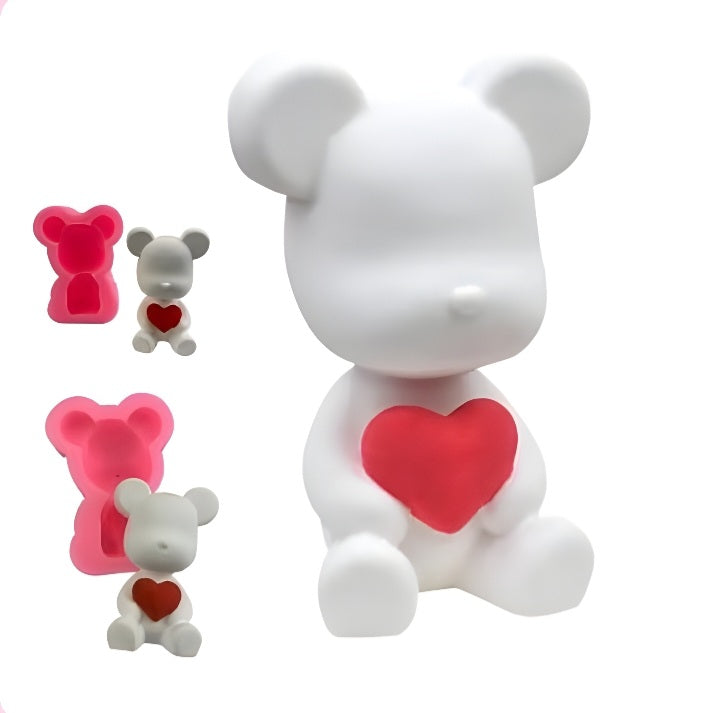 A 3D teddy bear silicone mold featuring a white teddy bear holding a red heart. The main bear is sitting and has a smooth finish, with rounded ears and a simplistic face. To the left, there are two smaller figures: one is a pink mold of the teddy bear, and the other is a smaller white bear with a red heart. The overall design is cute and playful, suitable for crafting and baking.