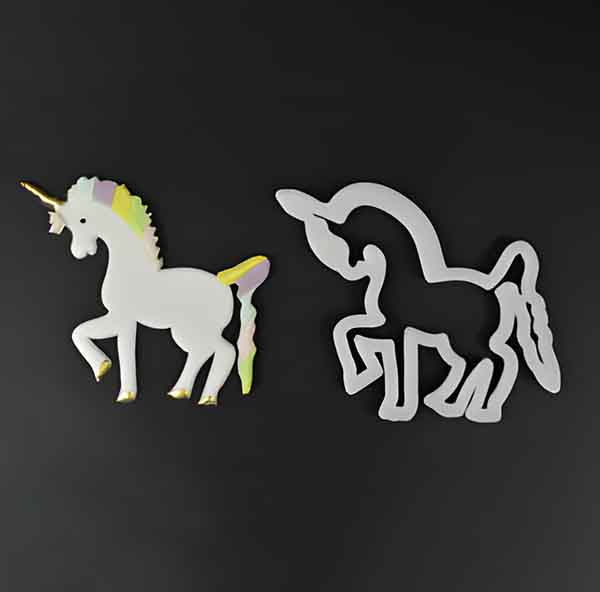 Image description for accessibility: Two unicorn-shaped cookie cutters are displayed against a black background. The left cutter is colorful, featuring a white unicorn with a multicolored mane and horn. The right cutter is a simple outline of a unicorn, shown in a solid light gray color. Both shapes are designed for creating cookie shapes.
