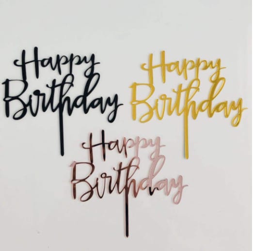The image features three acrylic cake toppers, each with the phrase "Happy Birthday" in a stylish cursive font. The toppers are displayed on a white background. The first topper is black, the second is gold, and the third is a rose gold color. Each topper has a thin stem for easy placement on cakes.