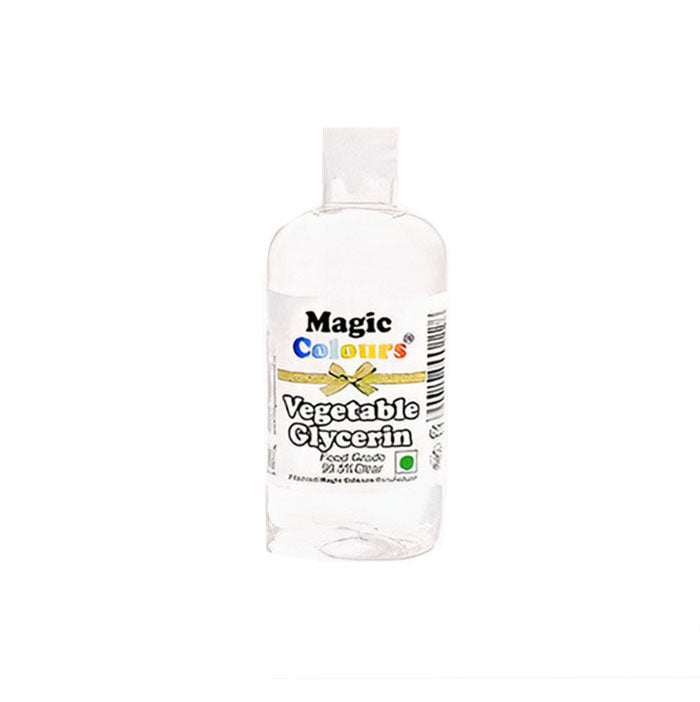A clear plastic bottle of "Magic Colours Vegetable Glycerin" is shown. The label features the product name in bold lettering, with a decorative bow graphic. The bottle is transparent, displaying the clear liquid inside, and it includes a barcode on the side. The packaging indicates that it is food grade.