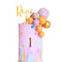 The image features a colorful birthday cake decorated with a variety of elements. At the top, there is a golden topper that reads "Renee." The cake itself has a pastel pink frosting base with a large number "1" prominently displayed on the front. The sides of the cake are adorned with numerous round cake decorations in shades of purple, orange, and gold, along with small, colorful sprinkles scattered throughout. The overall design is vibrant and festive, perfect for a birthday celebration.