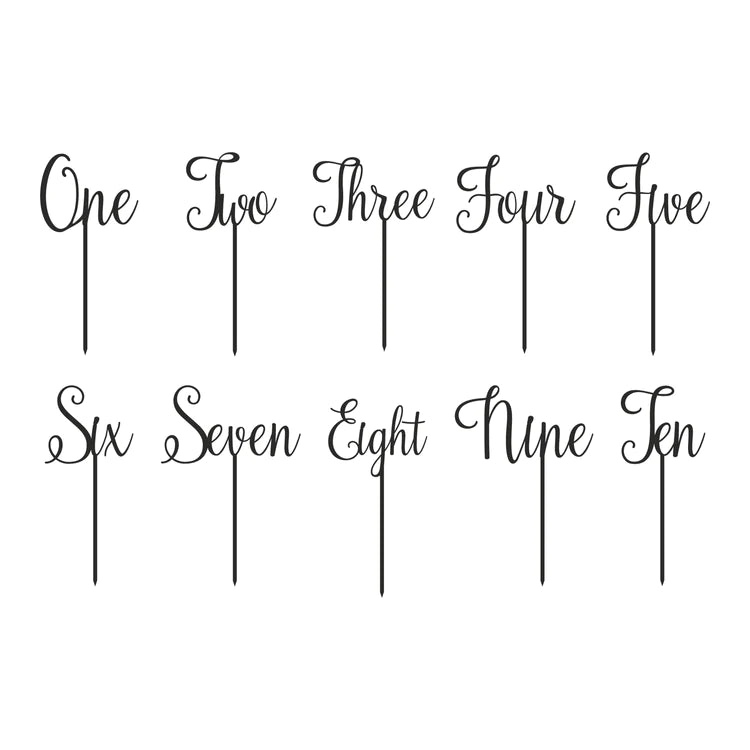 Image shows a collection of cake toppers designed for celebrating ages, featuring the words "One," "Two," "Three," "Four," "Five," "Six," "Seven," "Eight," "Nine," and "Ten" in an elegant, cursive font. Each word is attached to a slender stick for placement on a cake. The toppers are arranged in two rows, with five words in each row.