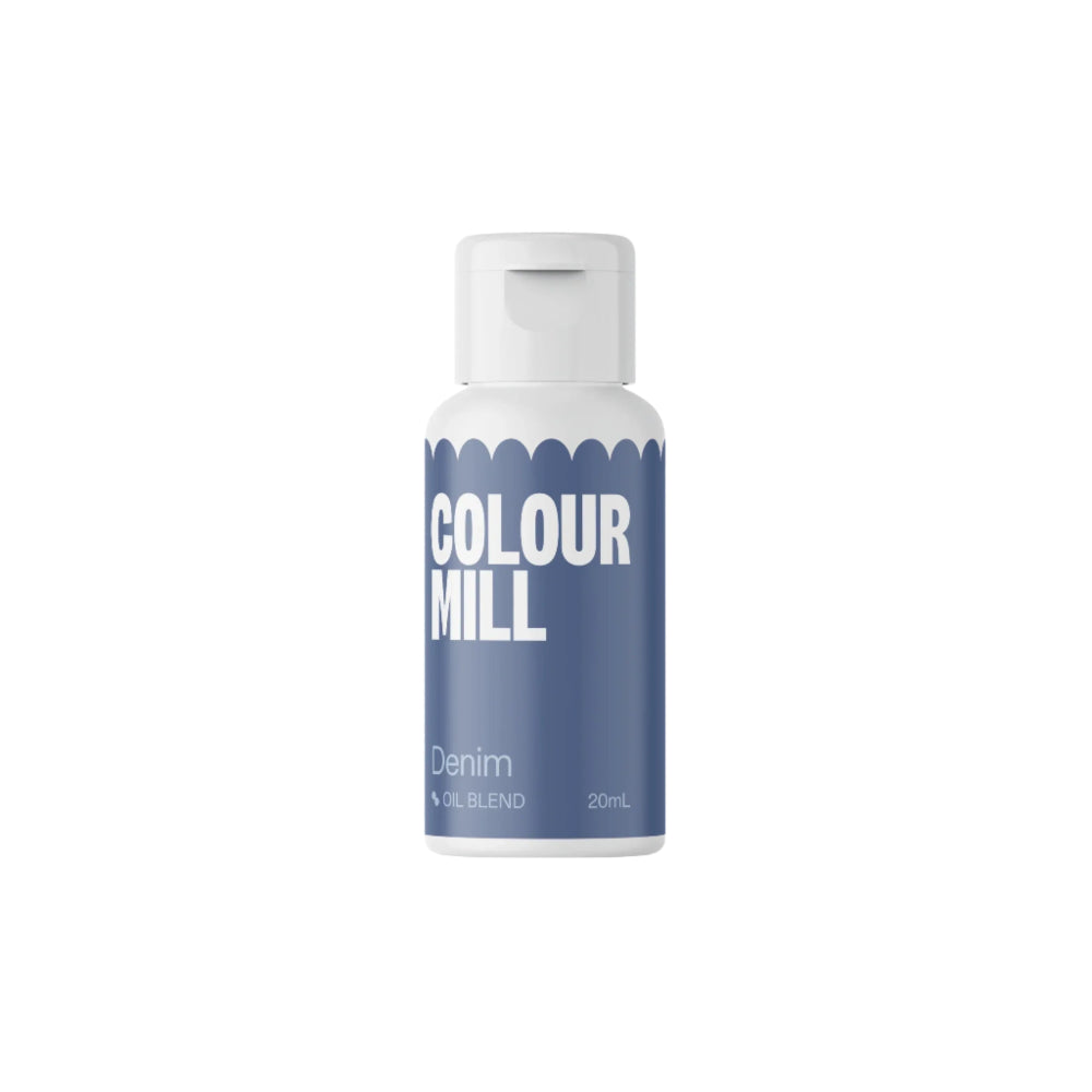 A bottle of Colour Mill oil-based food color is shown. The bottle has a white cap and a blue body with the words "COLOUR MILL" prominently displayed in white. Below the brand name, the label reads "Denim" and "Oil Blend," along with a volume indicator of "20mL." The design features a scalloped edge near the top of the bottle. The background is plain and dark, emphasizing the product.