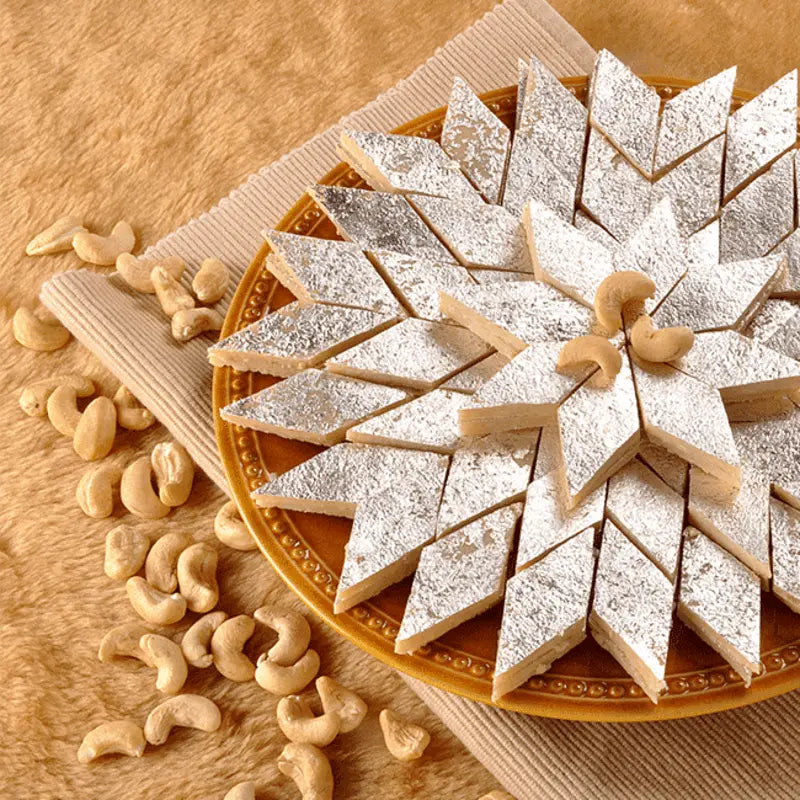 A plate featuring kaju katli, a sweet made from cashews, accompanied by whole cashew nuts for garnish.