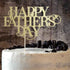 A cake with a smooth white frosting is topped with a decorative cake topper that reads "HAPPY FATHERS DAY" in an elegant golden script. The cake is adorned with black cookie crumbs and whole black Oreo cookies around the edges. The background features a textured, dark surface that contrasts with the cake and topper.
