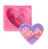 An image featuring a pink silicone mold in the shape of a heart, which has two hands forming a finger heart design inside it. Next to the mold is a completed purple silicone piece shaped like a heart, displaying the raised design of the two hands making the finger heart gesture.