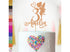 A decorative cake topper featuring a glittery fairy figure beside the number "3" and the name "Amelia," displayed on a white frosted cake. The cake is adorned with colorful heart-shaped sprinkles in shades of pink, blue, and yellow. To the left, a color palette of glitter cardstock options is shown in various vibrant hues, including gold, silver, black, and several shades of pink and purple. The background features soft, blurred decorations.