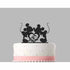 A white cake topped with a black acrylic cake topper featuring two cartoon mouse silhouettes, one holding hands with the other. At the center, there is a intertwined heart design. The cake has a pink ribbon around its base and is decorated with white fondant dots. The background is gray.