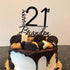 A round birthday cake topped with various types of cookies and chocolate decorations. Atop the cake is a black cake topper that reads "HAPPY 21st Brandon." The cake has a white frosting base with a dripping chocolate ganache effect. The decorations include Oreos, chocolate chip cookies, and waffle cones, all arranged artistically on the surface. The cake sits on a golden-colored cake board, with a neutral background.
