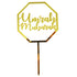 A gold acrylic cake topper in the shape of an octagon with the words "Umrah Mubarak" written in elegant, cursive font. It features a pointed stick at the bottom for easy placement on cakes or desserts.